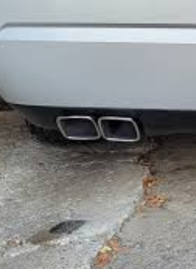Rear of a light grey Dodge Challenger in a parking structure showing two side-by-side rectangular custom exhaust tips.