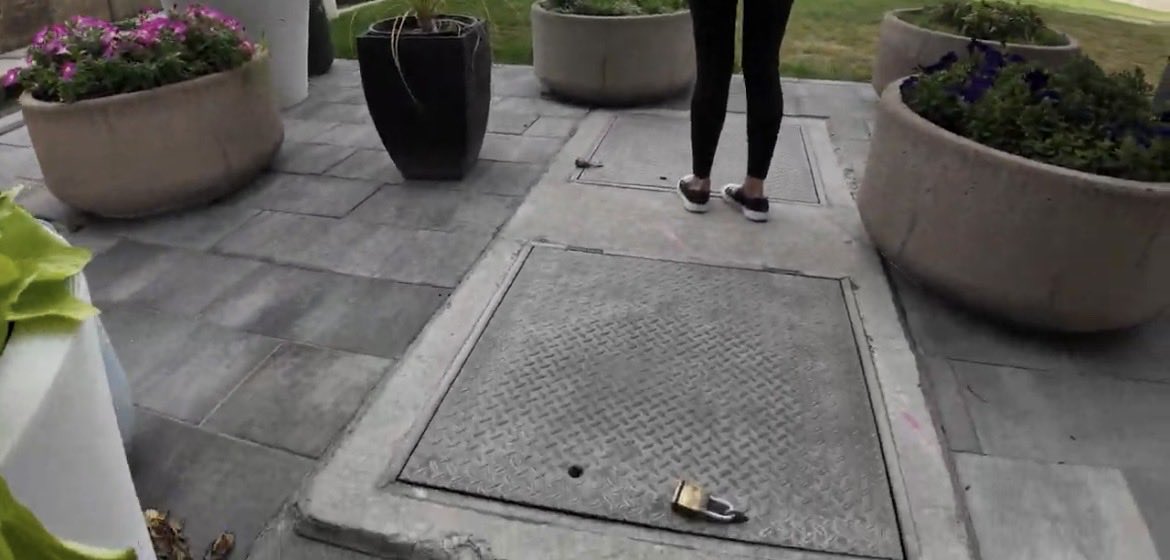 Two steel diamond-plate access doors set flush into new grey pavers between concrete planters in the UVU courtyard, with a brass padlock lying open on the nearer door