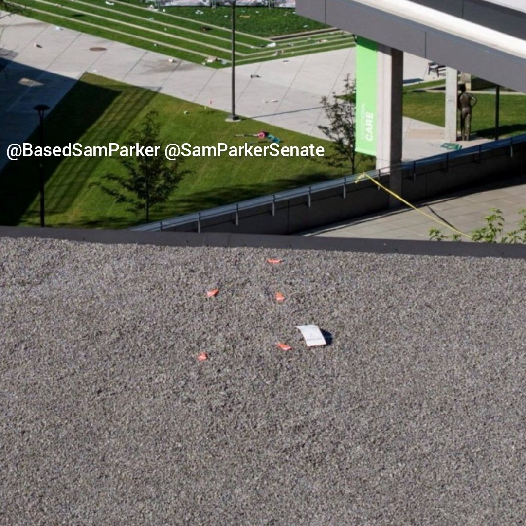 Photograph across the gravel surface of the Losee Center roof showing orange evidence markers and a white placard, with the UVU courtyard and a strand of yellow tape visible beyond the roof edge