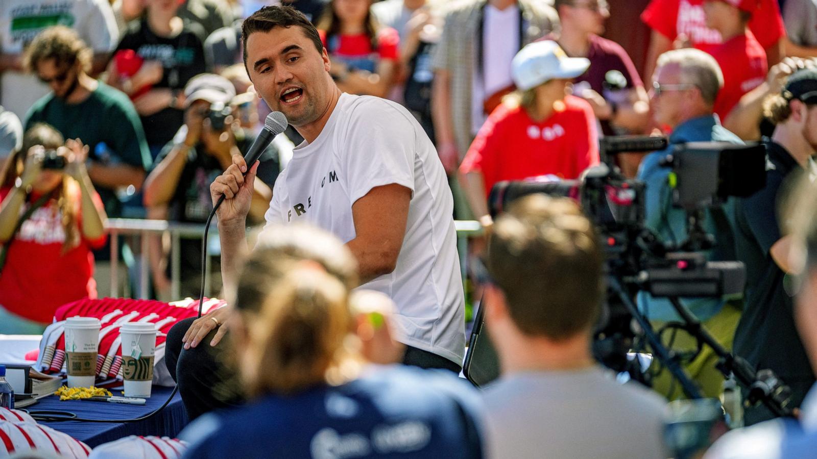 This eye-level, medium-shot photograph captures Charlie Kirk speaking into a microphone at an outdoor public event.