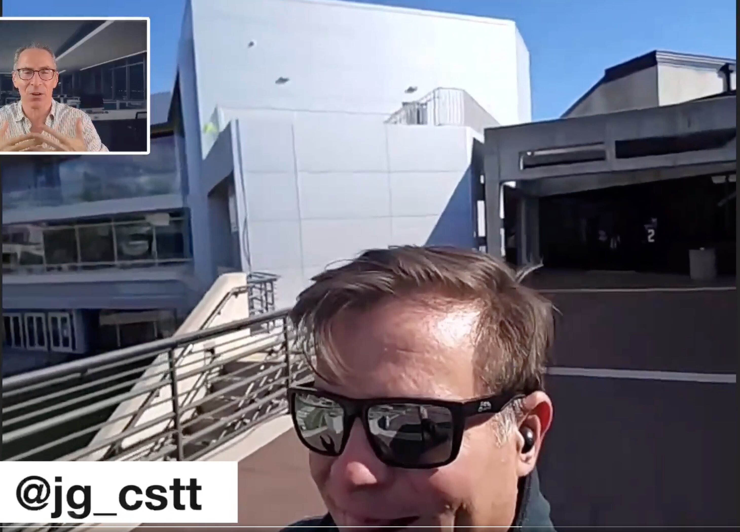 This is a video screenshot showing a close-up of a man filming himself outdoors on what appears to be a modern school, university, or corporate campus.